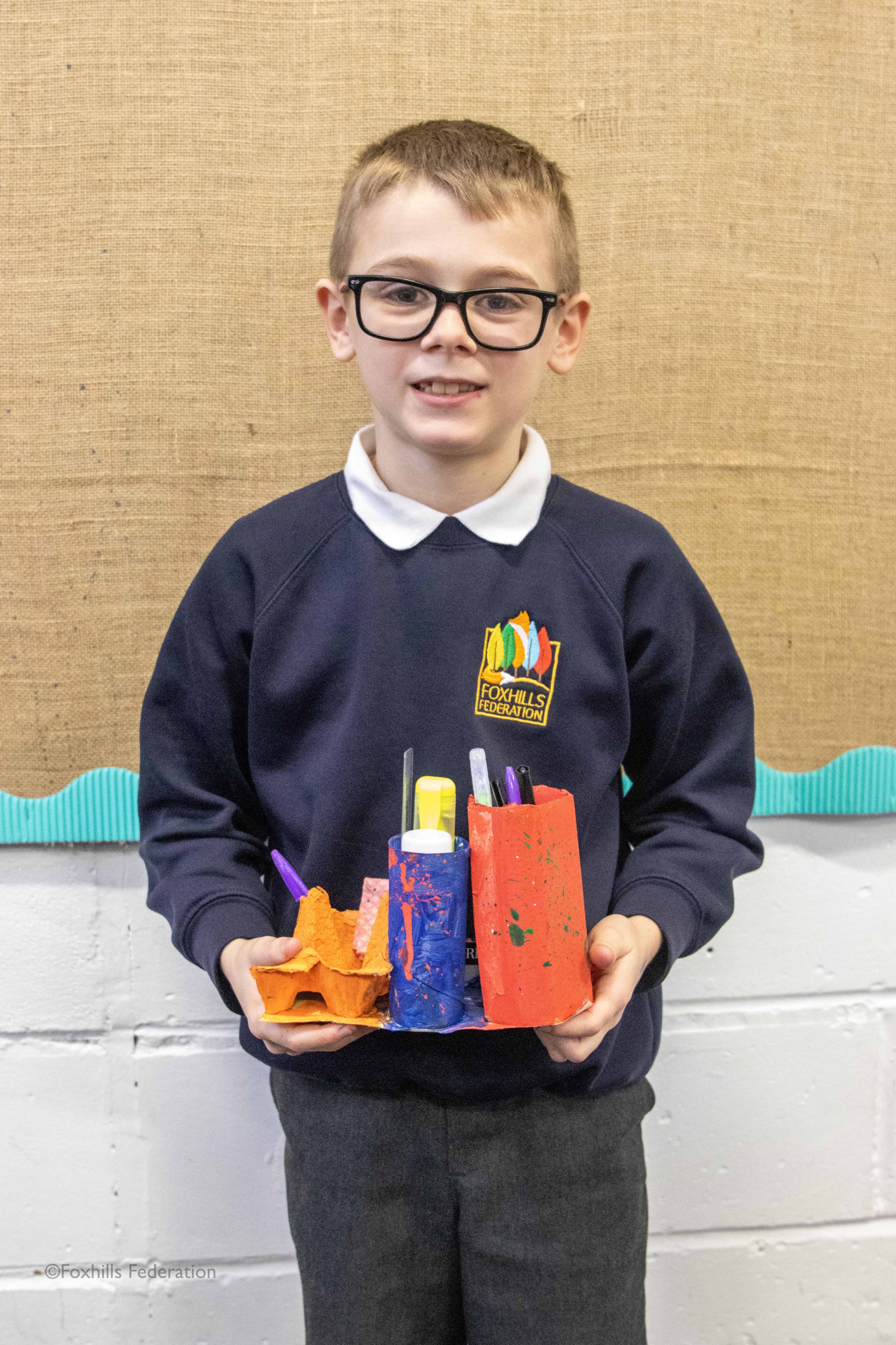 A boy smiles and holds a homemade desk tidy.