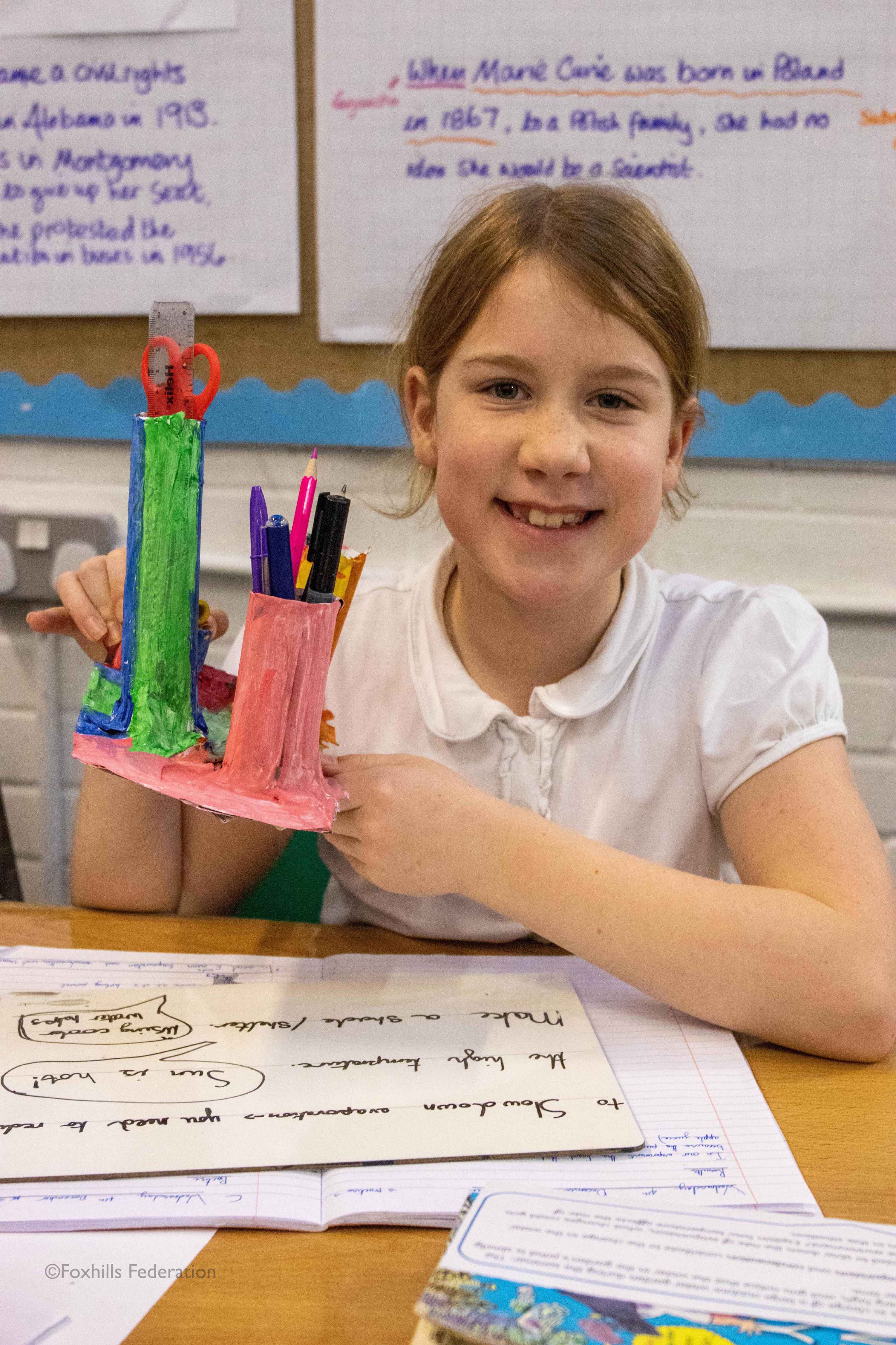 A girl smiles and holds a homemade desk tidy.