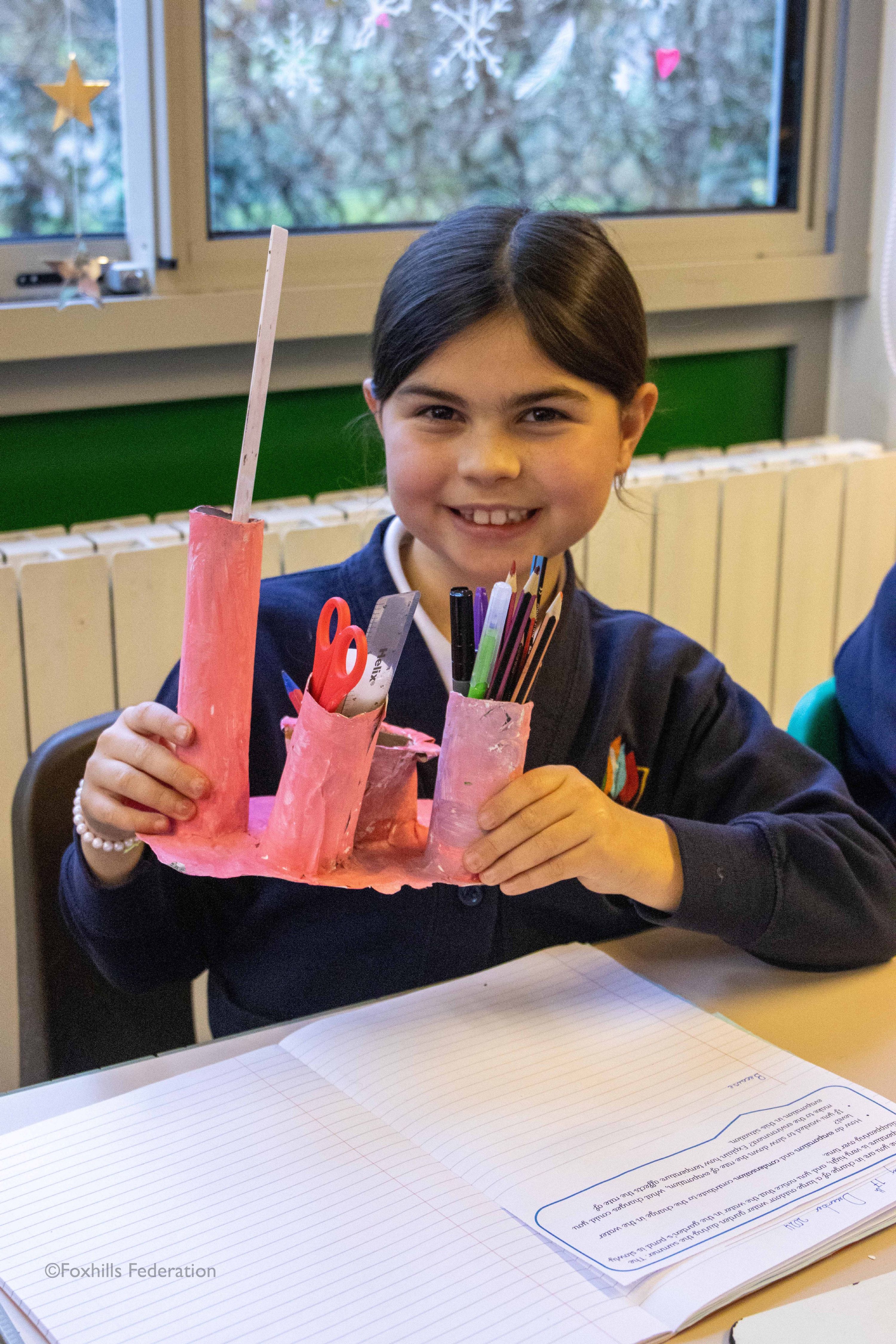 A girl smiles and holds a homemade desk tidy.