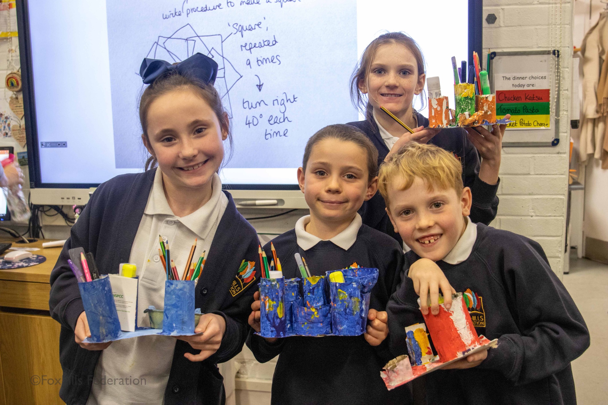 Children smile and hold homemade desk tidies.