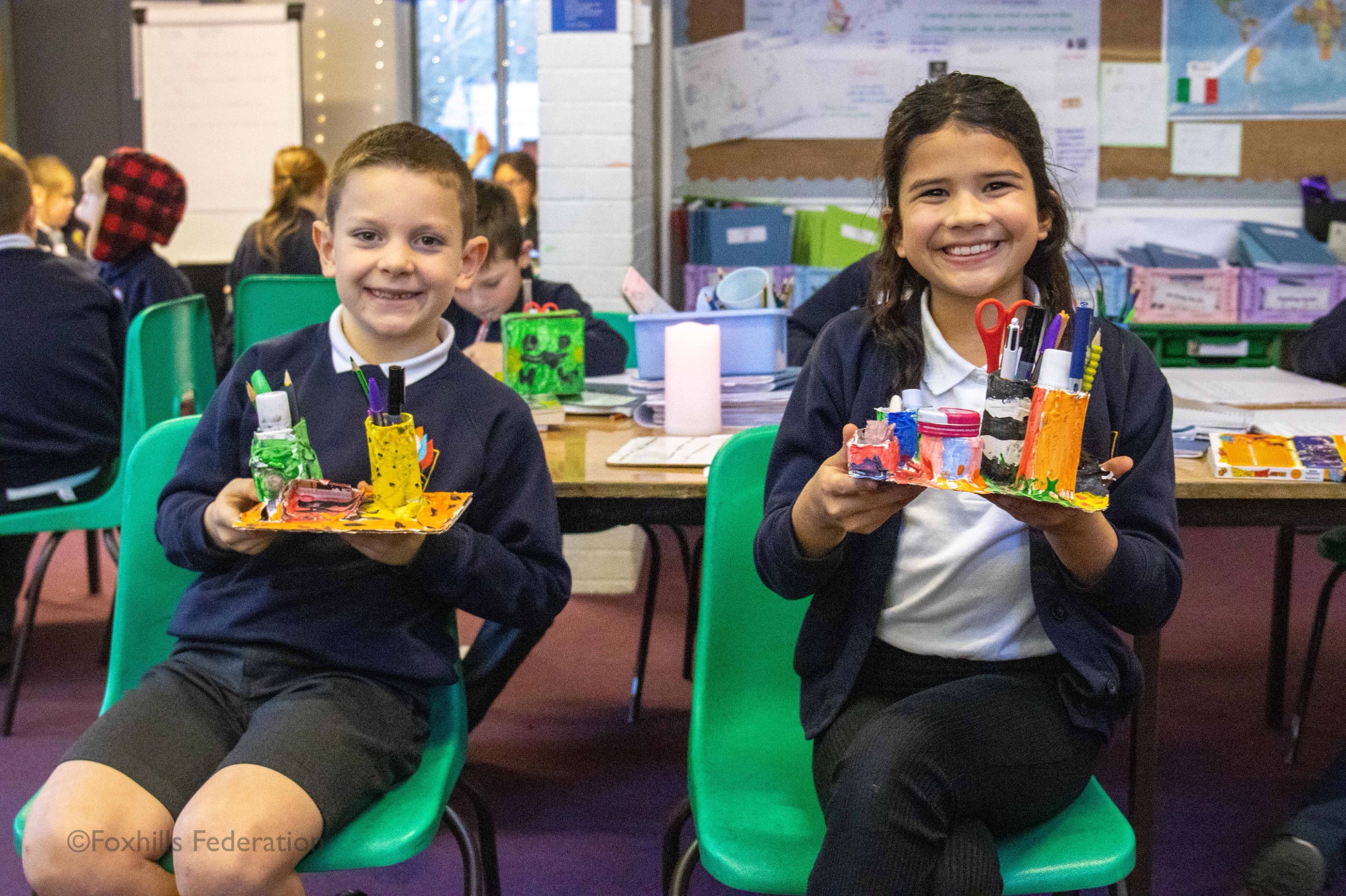 Children smile and hold homemade desk tidies.