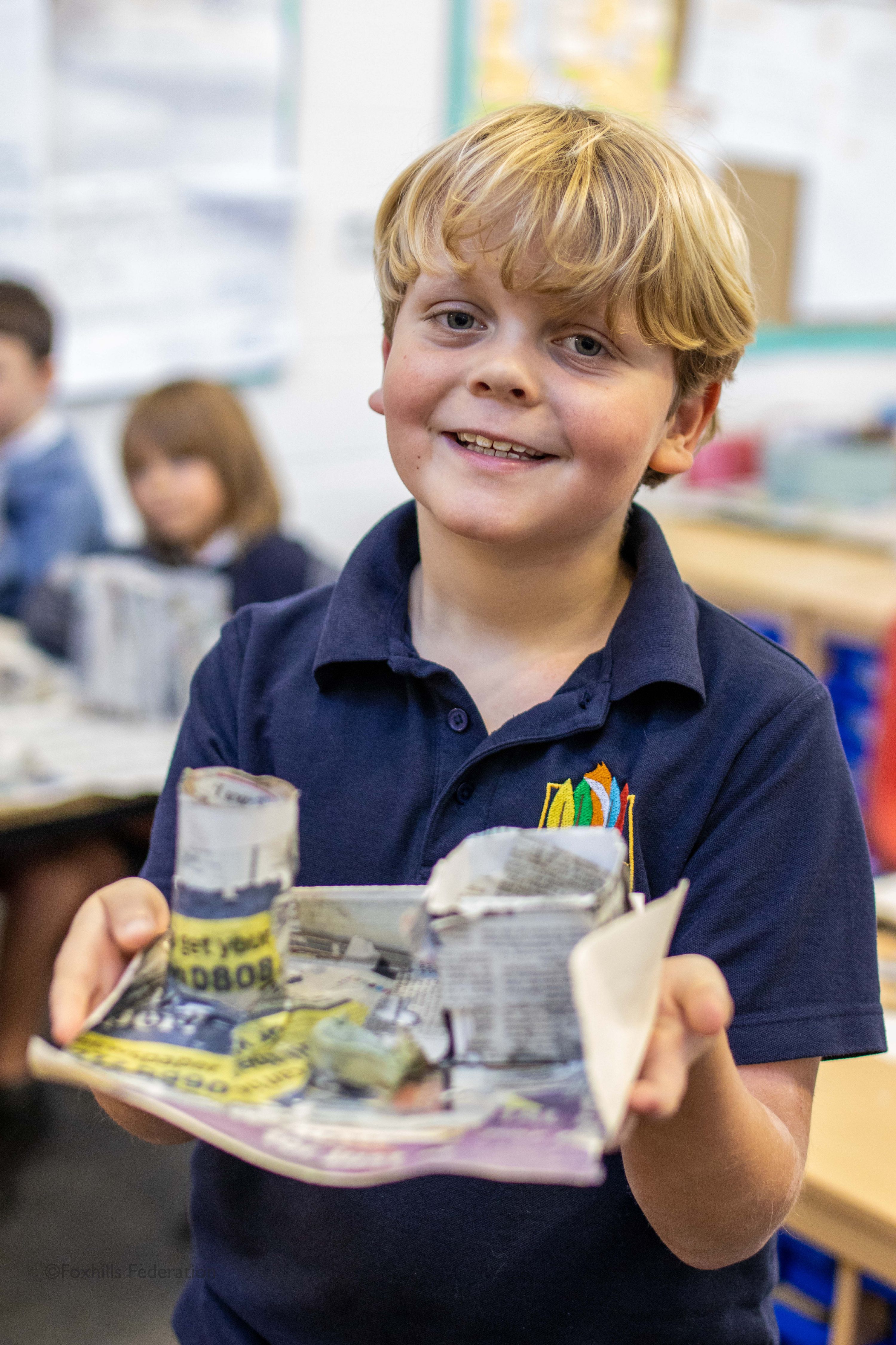 A boy smiles and holds a homemade desk tidy.