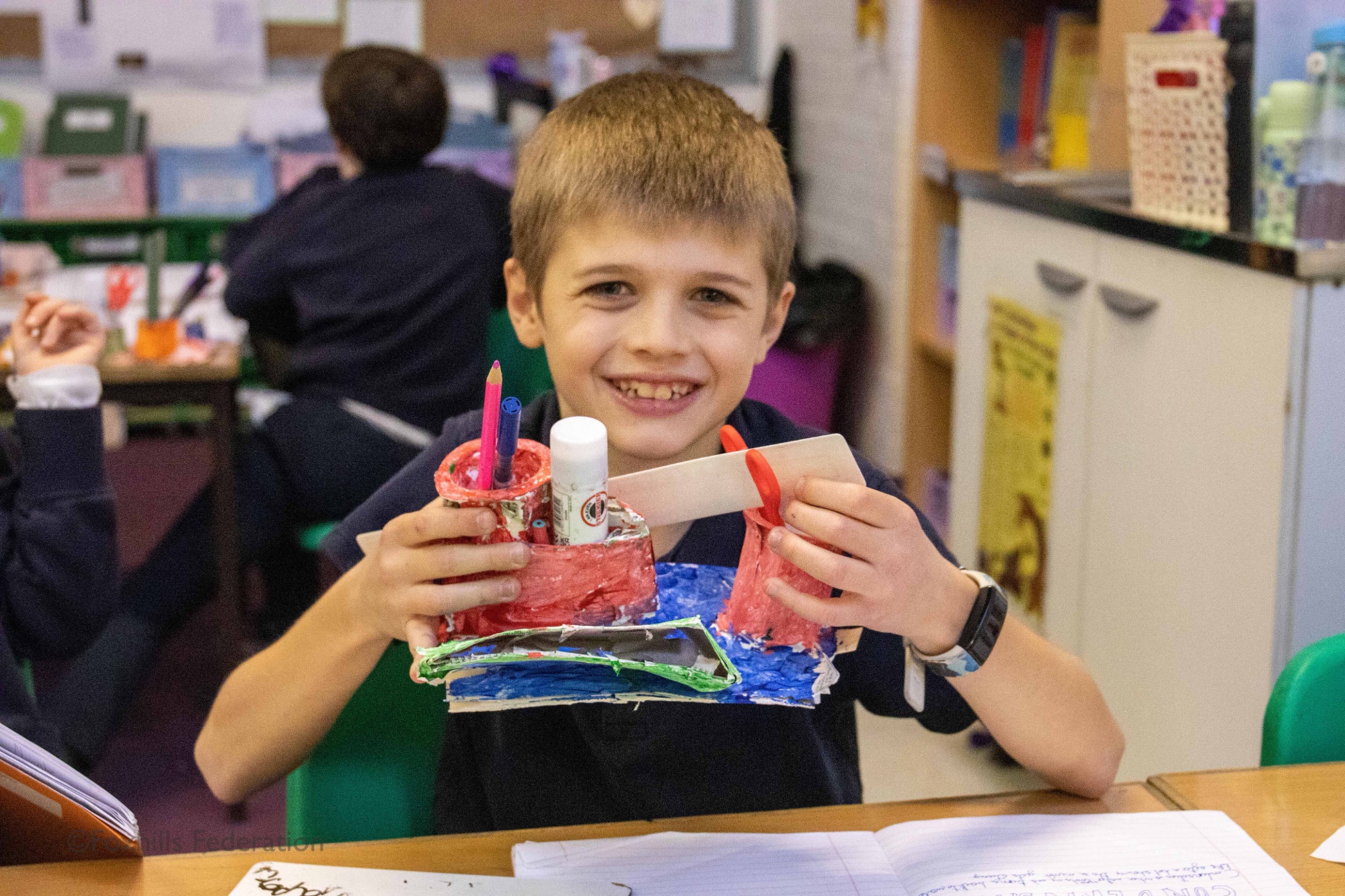 A boy smiles and holds a homemade desk tidy.