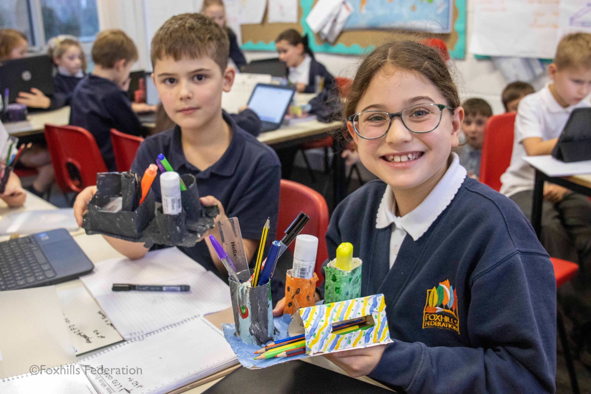 Children smile and hold homemade desk tidies.