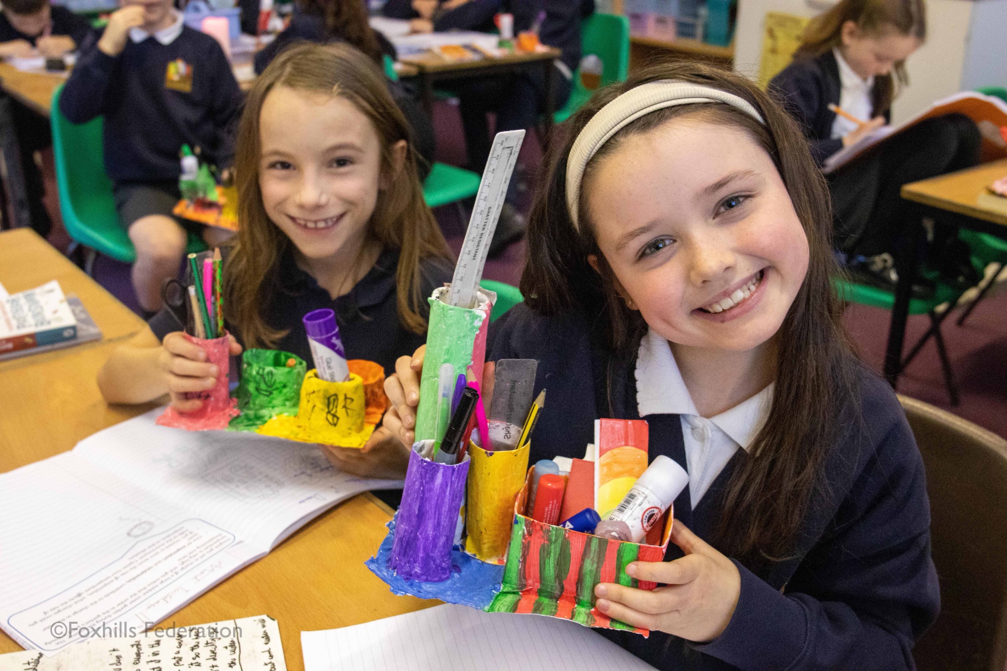 Children smile and hold homemade desk tidies.